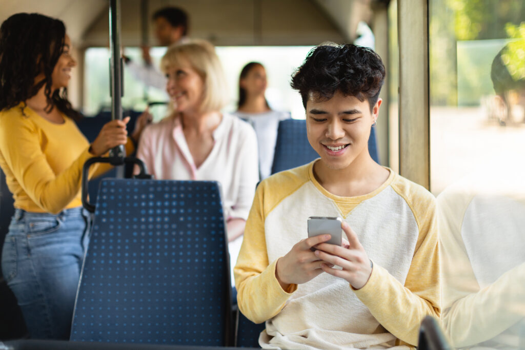 Ein junger Mann benutzt sein Smartphone im Bus.