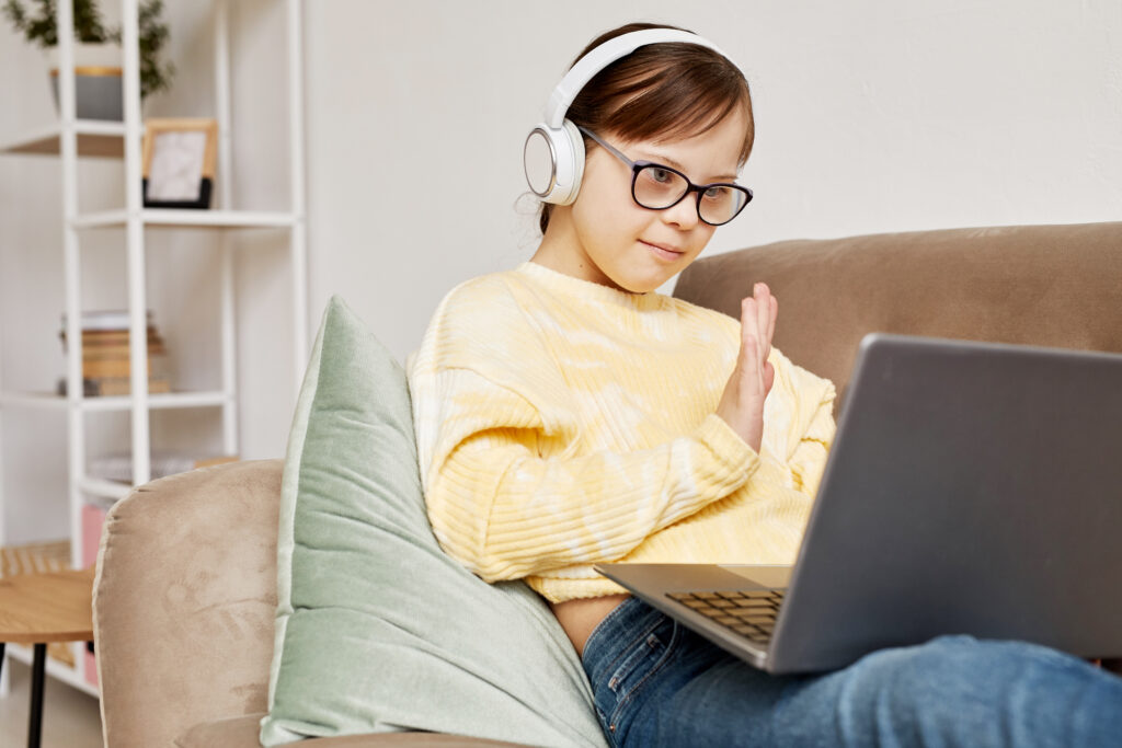 Ein Mädchen mit Down-.Syndrom sitzt mit ihrem Laptop und Kopfhörern auf der Couch.